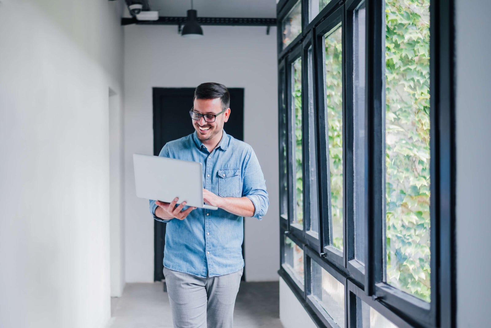 businessman in glasses walks down office hallway with laptop