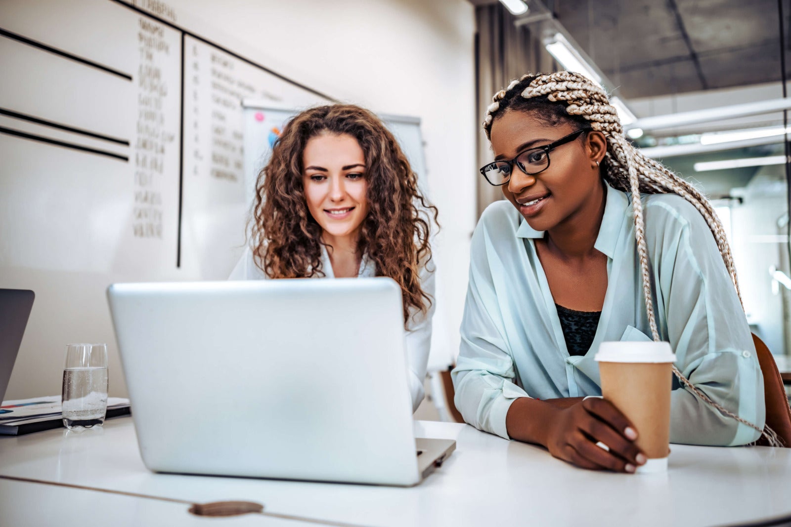 two diverse businesswomen looking at laptop with coffee