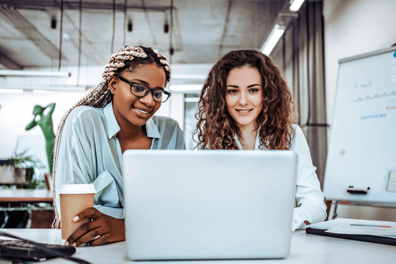 two diverse colleagues look at laptop together in office